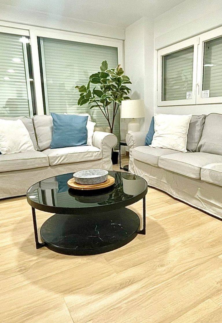 salon iluminado con sofas grises, mesa de centro de granito negro, suelo color mader natural y de fondo una planta muy bonita